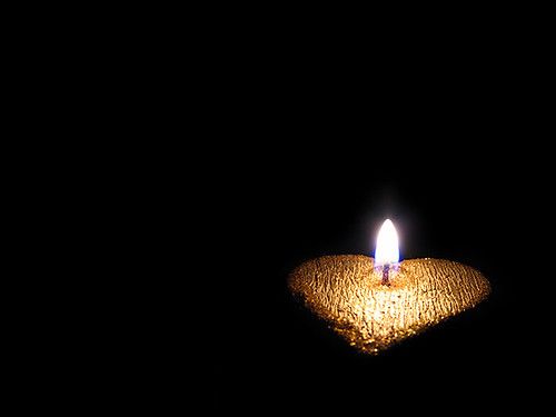 A small lit candle resting on a gold heart-shaped dish