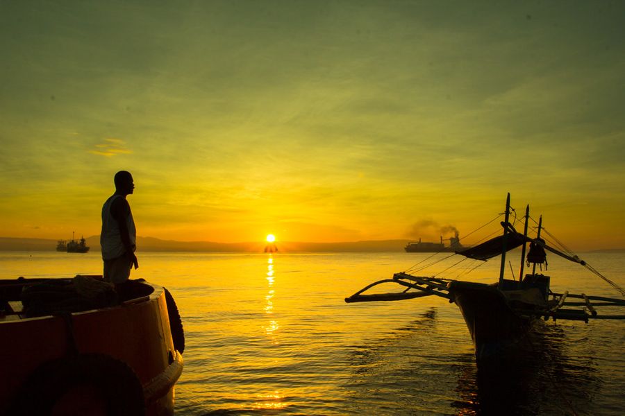 A small boat silhouetted against a golden sunrise on calm water
